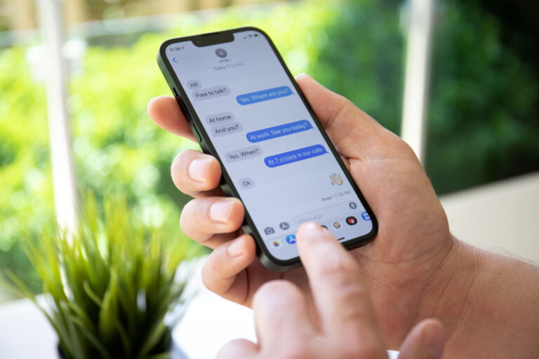 Osoba trzyma smartfon wyświetlający wymianę wiadomości tekstowych na tle roślinności w aplikacji iMessage.