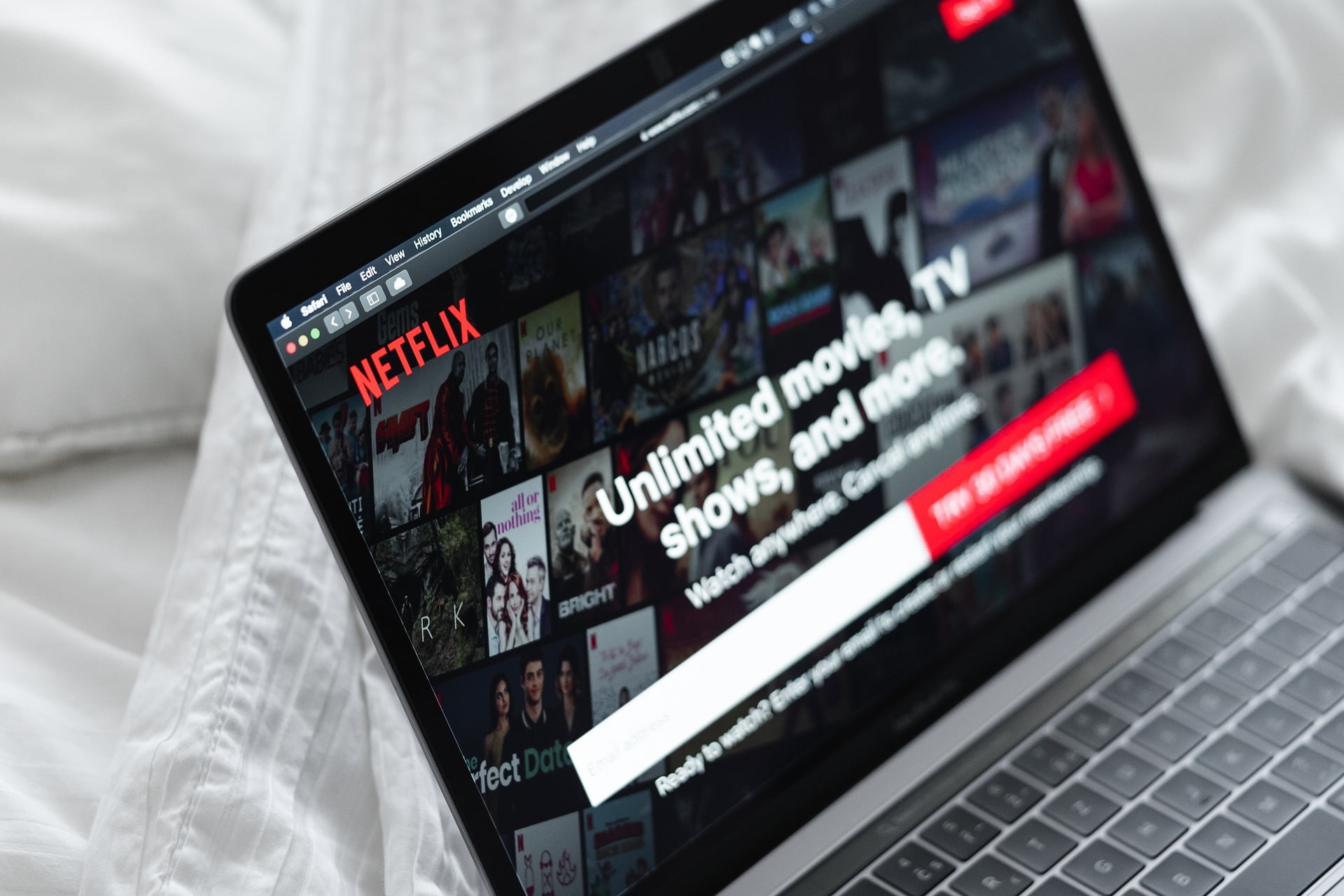 Strona Netflix otworzona na laptopie. Laptop leży na łóżku i białej pościeli