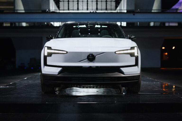 Biały samochód elektryczny marki Volvo stojący na scenie z włączonymi przednimi światłami LED.