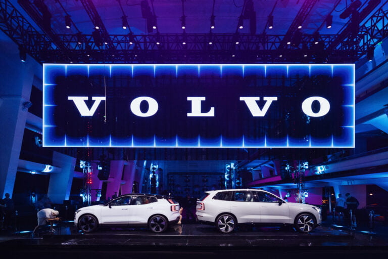 Prezentacja samochodów marki Volvo na wystawie motoryzacyjnej z dużym logo Volvo w tle podświetlonym na niebiesko.