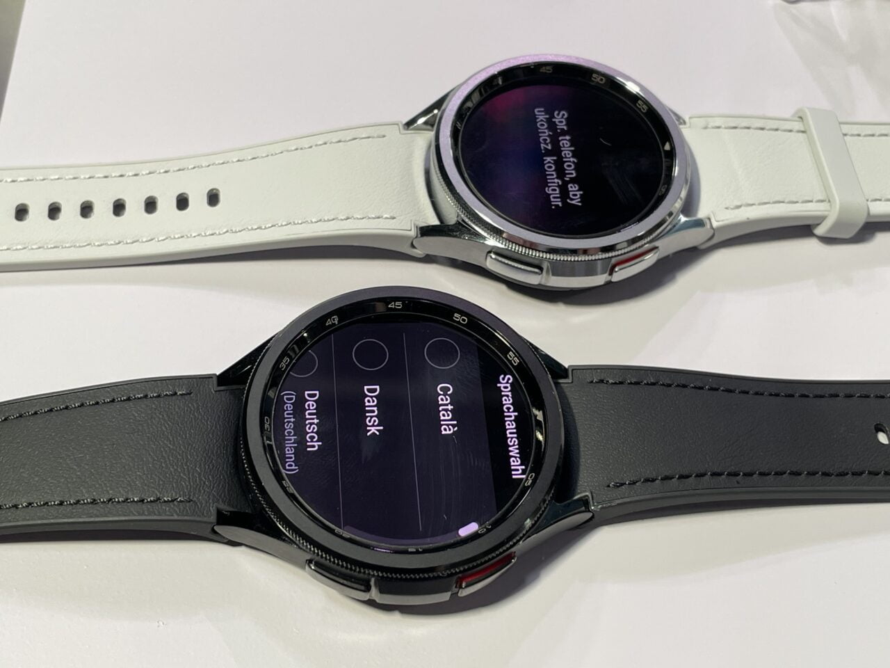 Dwa inteligentne zegarki z paskami - jeden z białym paskiem i czarnym wyświetlaczem, a drugi z czarnym paskiem i wyświetlaczem pokazującym opcje językowe.