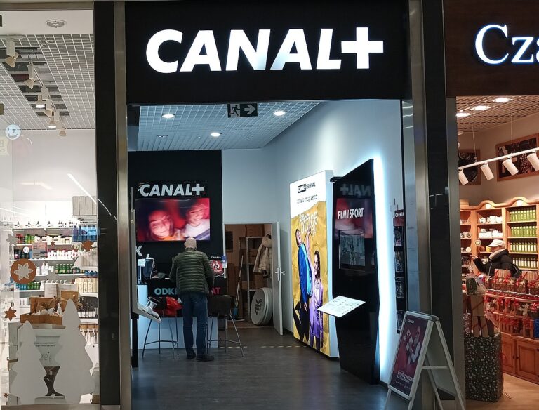 Wejście do sklepu CANAL+ w centrum handlowym z wyświetlaną reklamą na ekranie, przy którym stoi klient.