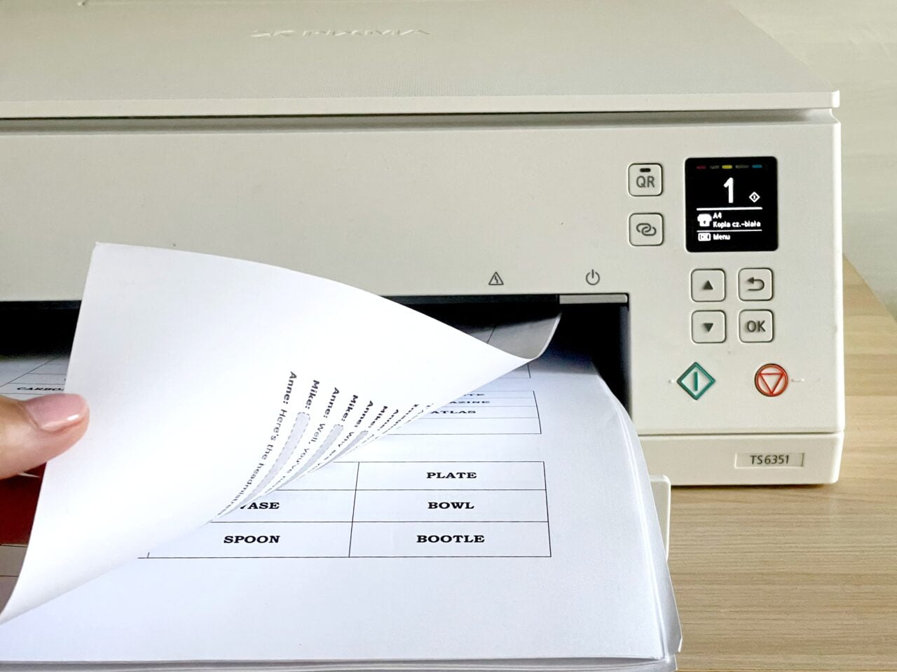 Dłoń osoby wyjmującej wydrukowane arkusze papieru z biurowego urządzenia wielofunkcyjnego. Przykład na druk dwustronny