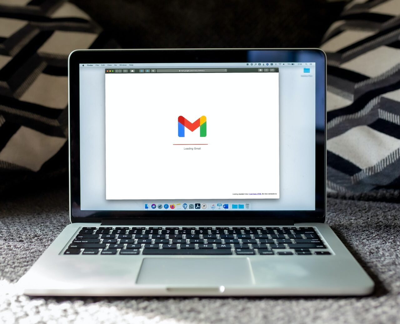 Laptop na dywanie pokazujący ekran ładowania usługi Gmail.