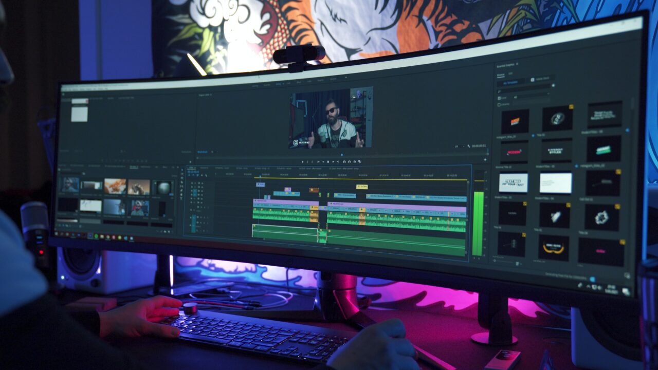 Osoba pracująca przy montażu wideo na profesjonalnym oprogramowaniu edycyjnym na szerokim monitorze w oświetlonym na niebiesko pomieszczeniu.