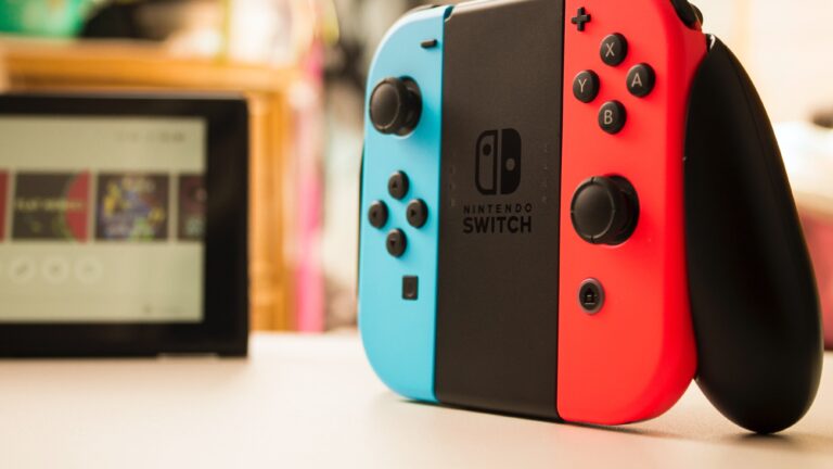 Konsola do gier Nintendo Switch z niebieskim i czerwonym kontrolerem Joy-Con, rozmyty obraz urządzenia w tle.