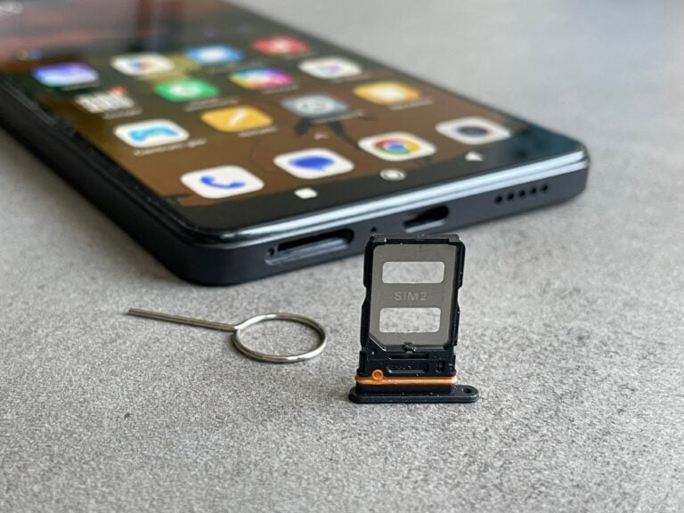 smartfon redmi note 12 leżący z włączonym ekranem na płaskiej powierzchni, przed nim tacka na karty SIM z kluczykiem