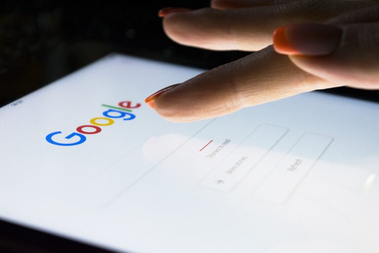 Dłoń dotyka ekranu tabletu z wyświetloną stroną główną wyszukiwarki Google.