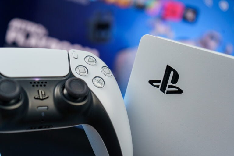 Pad do gier DualSense PlayStation 5 na pierwszym planie z rozmytym tłem gdzie widnieje logo PlayStation.