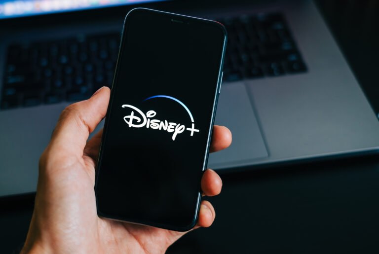 Smartfon z logo Disney+ na ekranie. W tle widoczny laptop