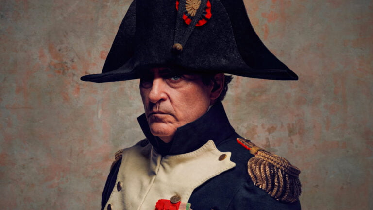 Mężczyzna w historycznym mundurze wojskowym z czarnym trójrożnym kapeluszem, patrzący poważnie z dystynkcjami na ramieniu, na tle odcieni beżu.