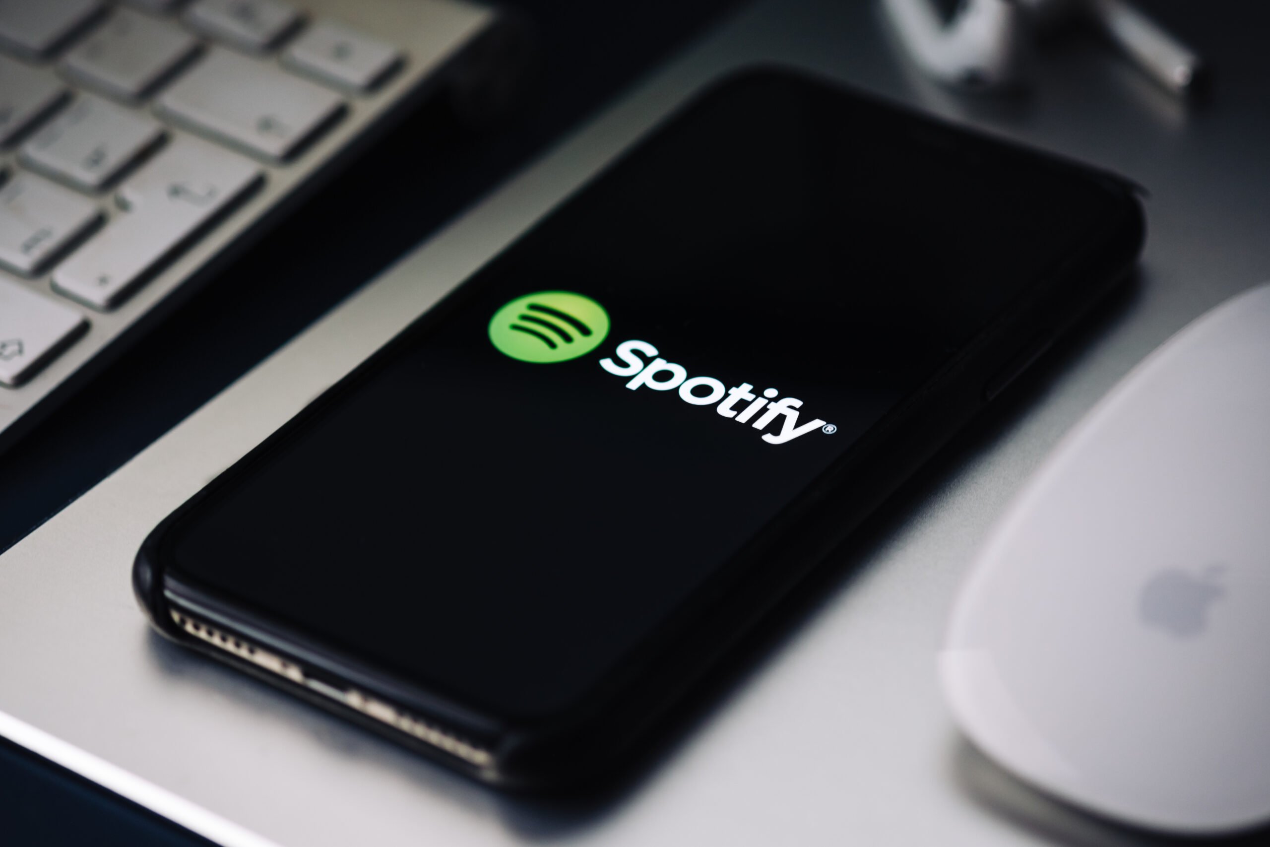 Czarny smartfon z logo Spotify na ekranie, położony na laptopie obok białej myszki komputerowej.