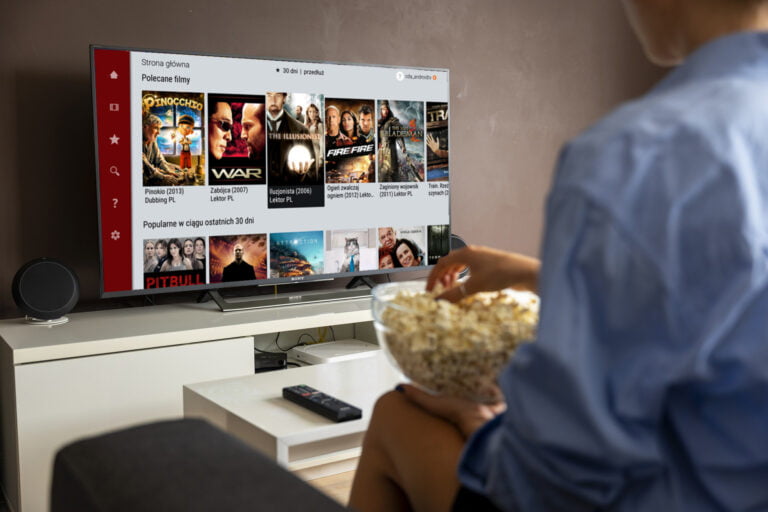 Osoba siedzi na kanapie z miską popcornu, oglądając wybór filmów na ekranie telewizora w salonie, gdzie widać ekran z CDA Premium.