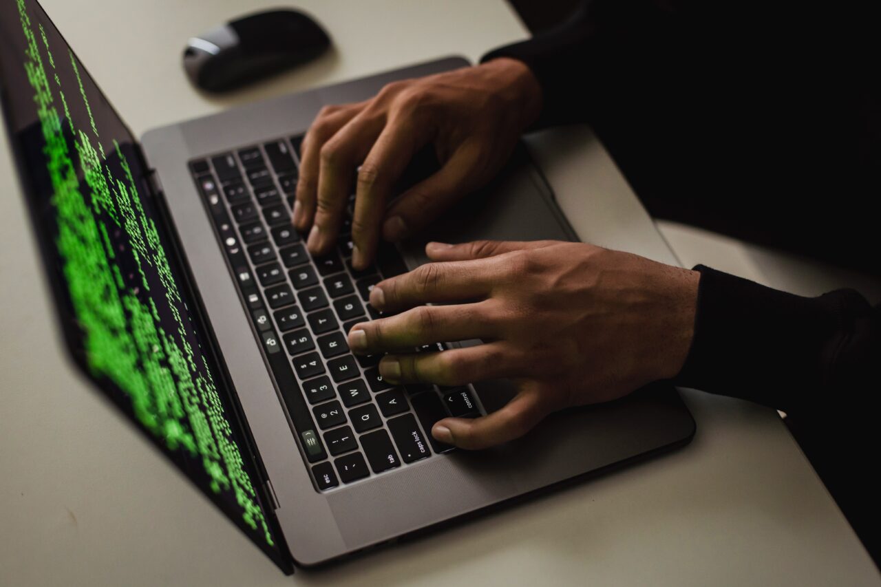 haker, człowiek piszący na klawiaturze laptopa, na ekranie którego widać zielone znaki i największy wyciek danych