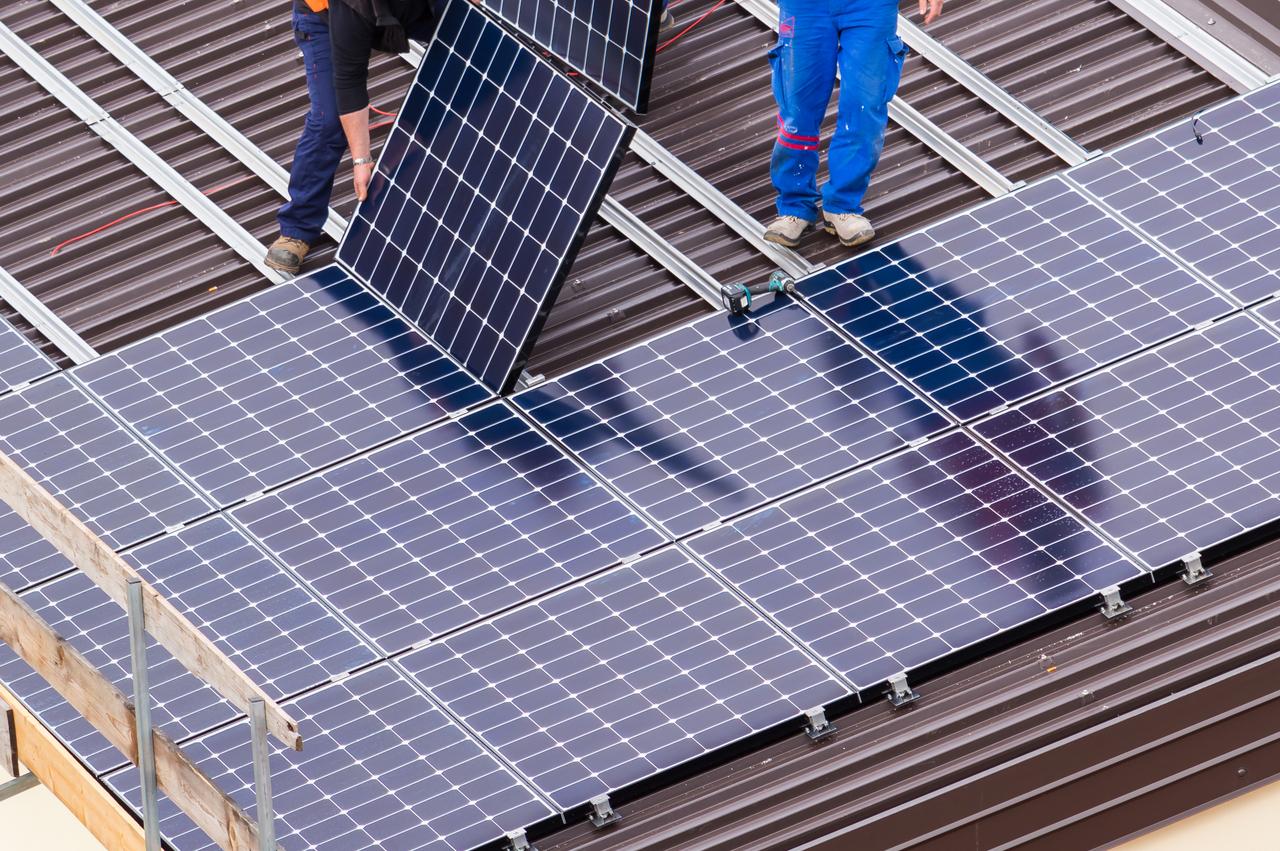 Dwóch techników instaluje panele słoneczne na dachu budynku.