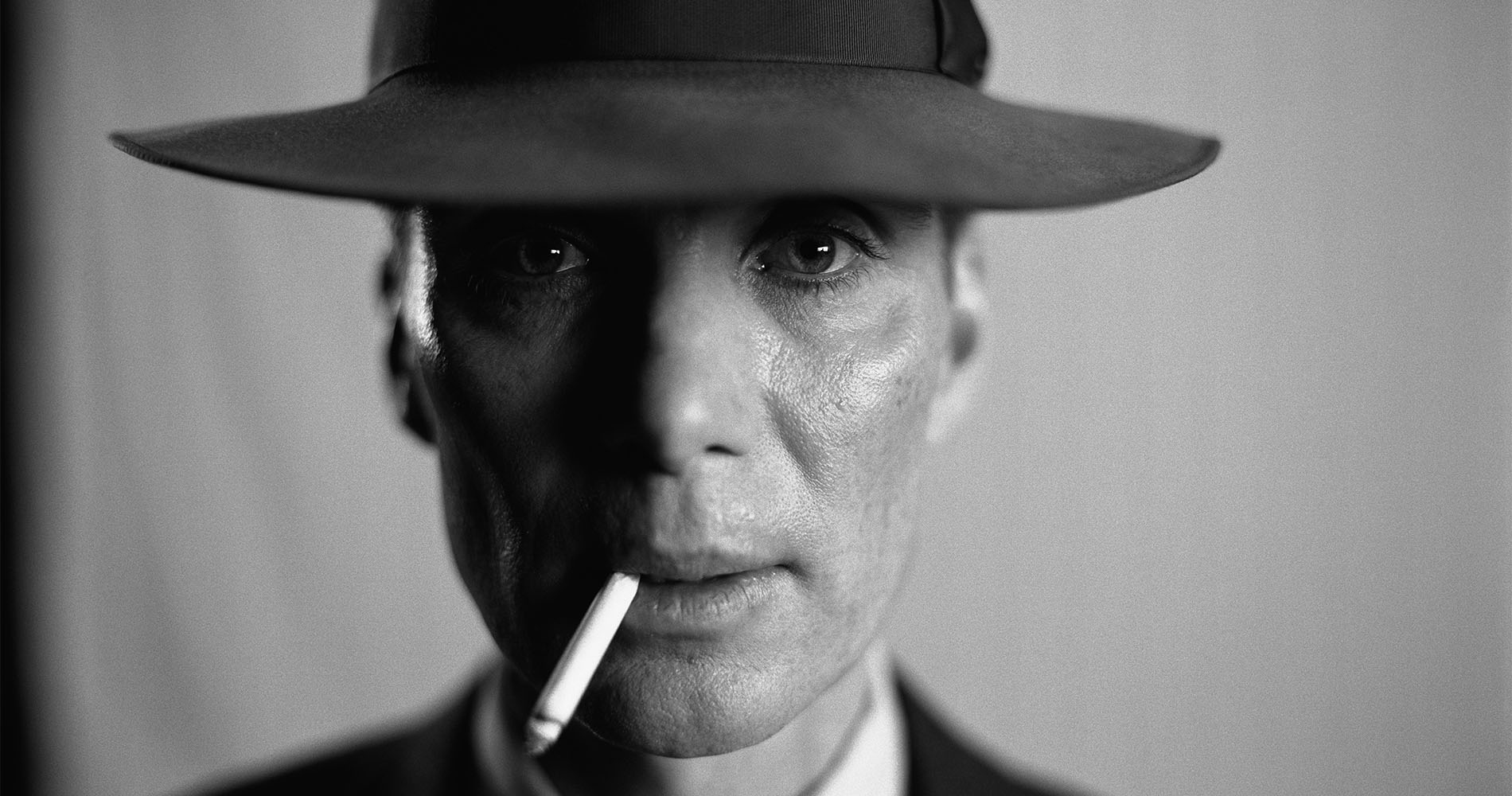Czarno-białe zdjęcie portretowe mężczyzny w kapeluszu z papierosem w ustach.