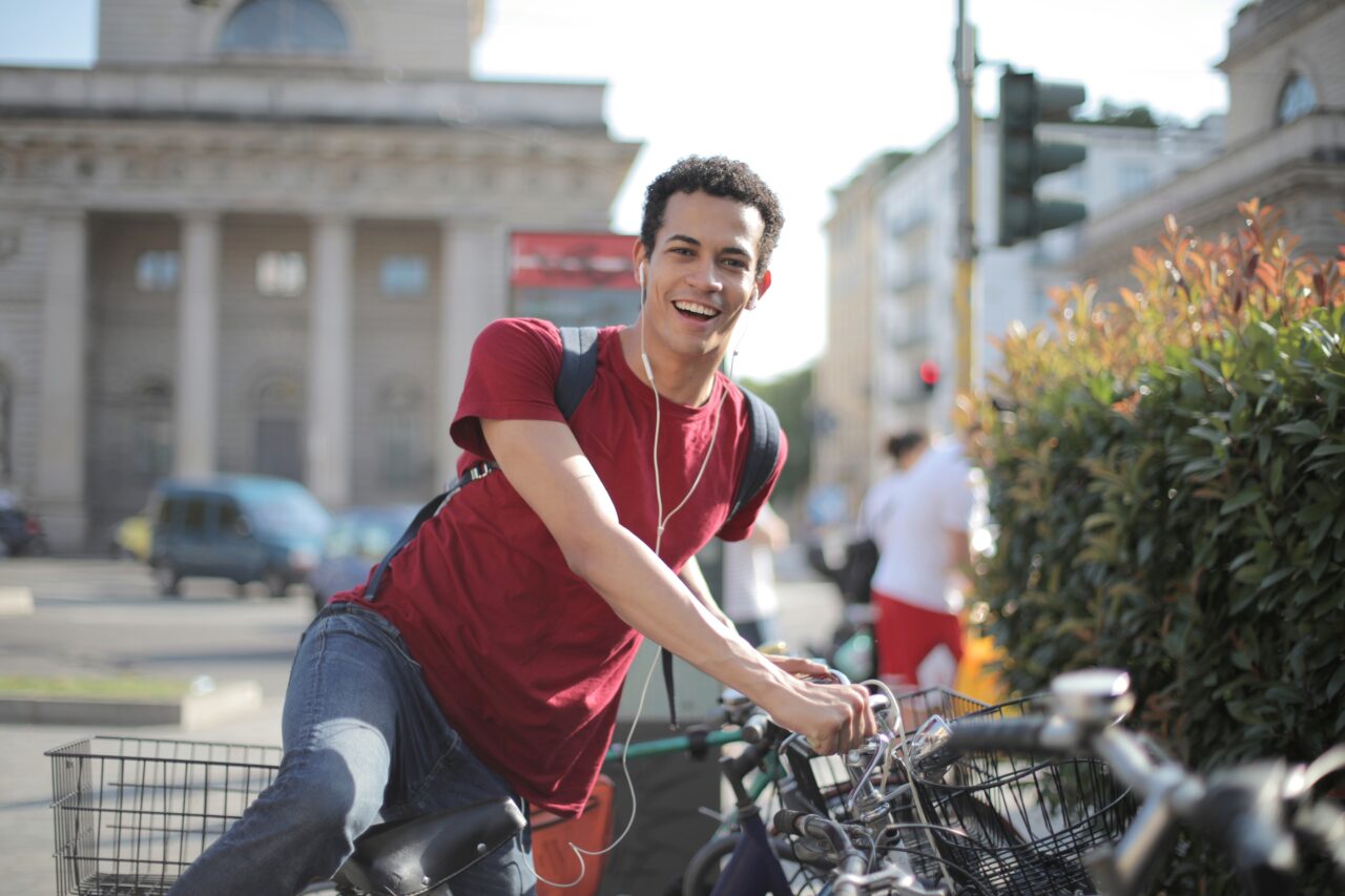 Młody mężczyzna uśmiecha się i opiera się o rower na miejskiej ulicy w słoneczny dzień.
