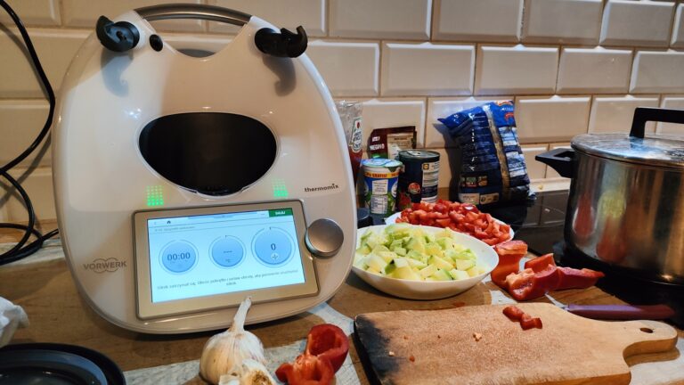 Robot kuchenny Thermomix na blacie kuchennym obok talerzy z pokrojonymi warzywami i deską do krojenia z resztkami papryki.