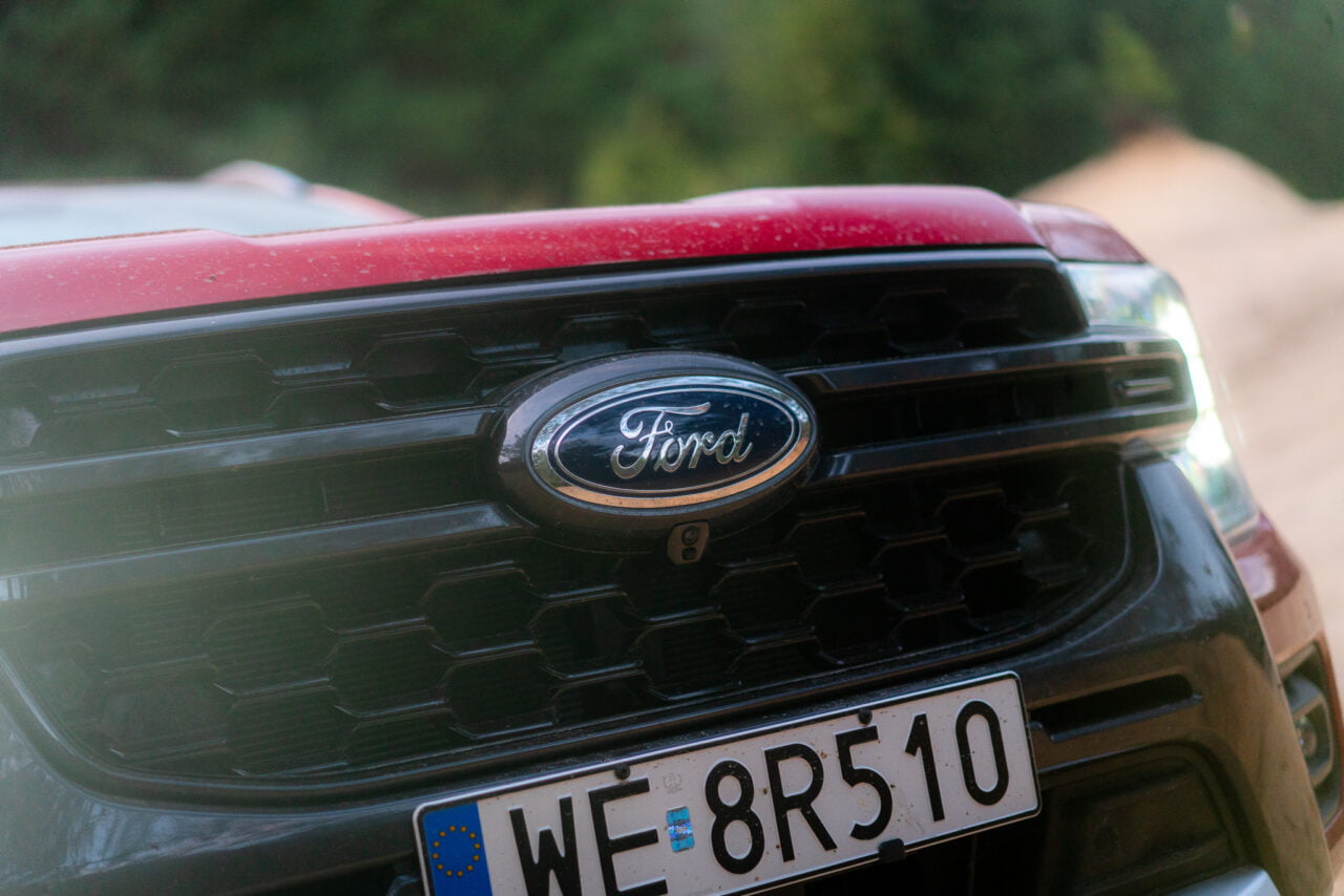 Częściowy przód czerwonego samochodu marki Ford z widocznym logo i rejestracją europejską.