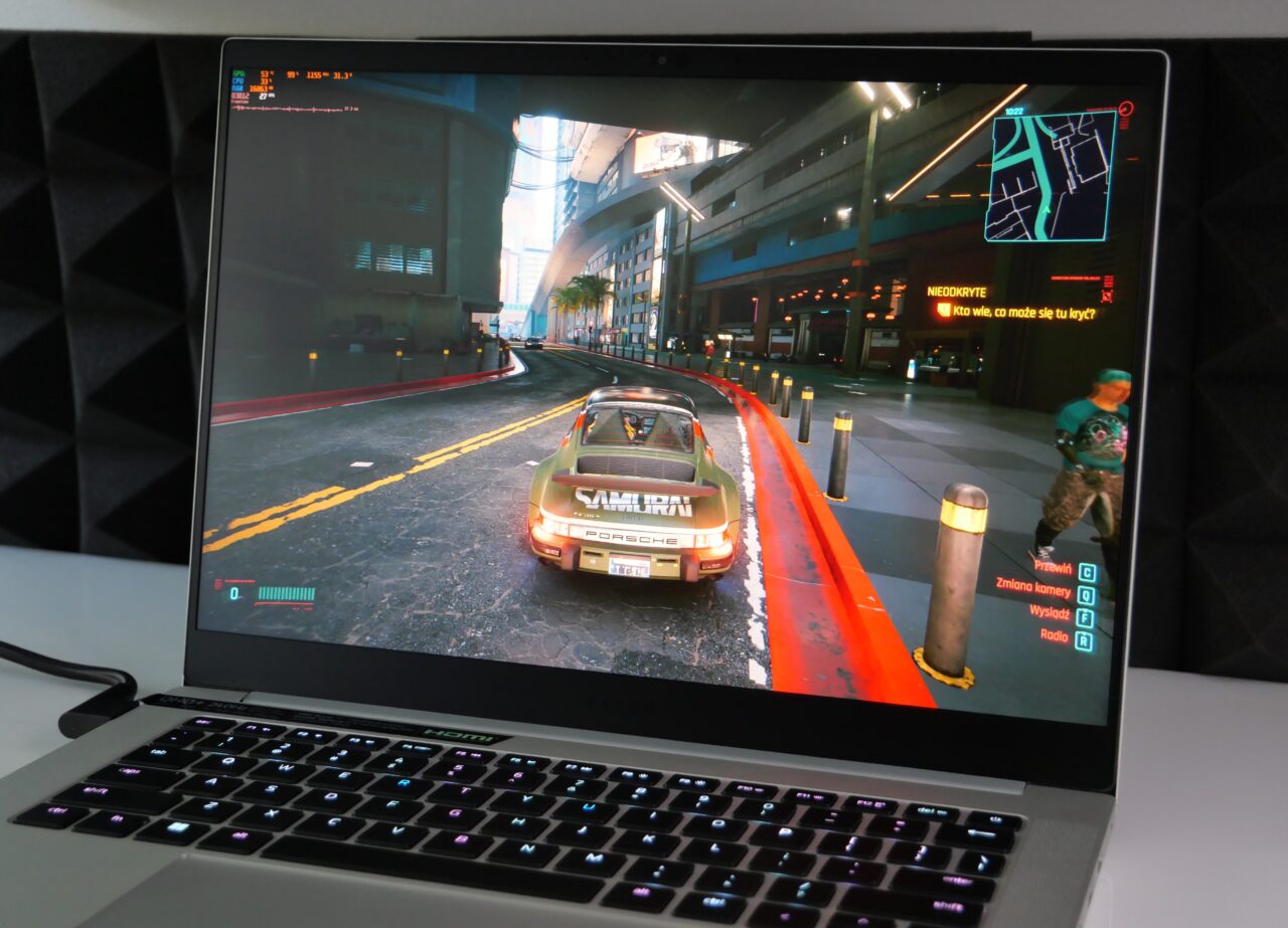 Zdjęcie laptopa na biurku wyświetlającego grę wideo z samochodem jadącym przez miejską ulicę.