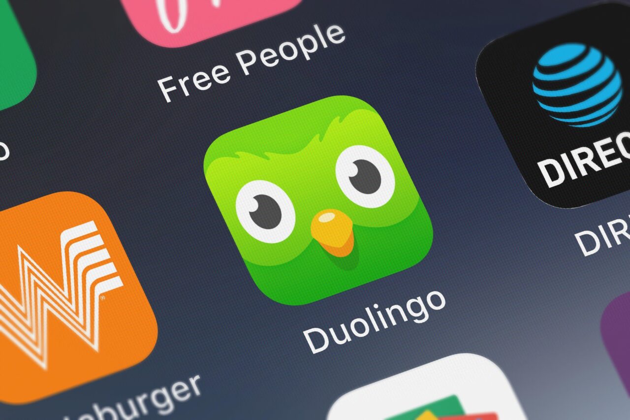 Ikona aplikacji Duolingo z zieloną sową na wyświetlaczu smartfona, w otoczeniu innych ikon aplikacji.