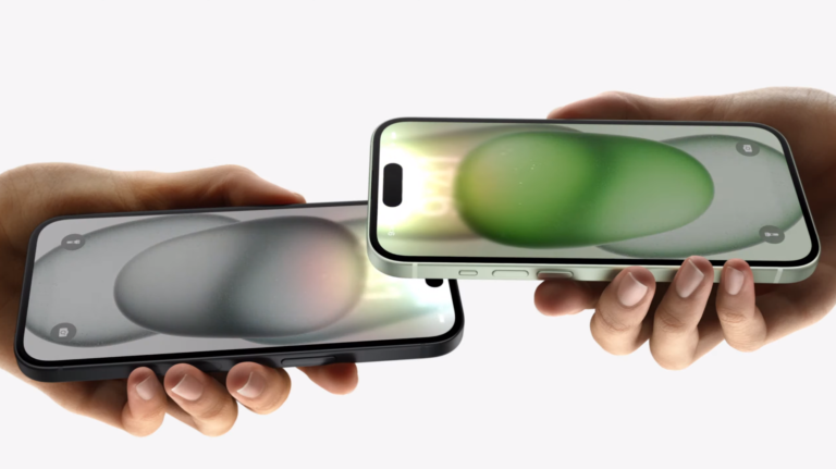 Dłonie trzymające dwa smartfony naprzeciw siebie, z ekranami wyświetlającymi rozmyte abstrakcyjne tła w odcieniach szarości i zieleni.