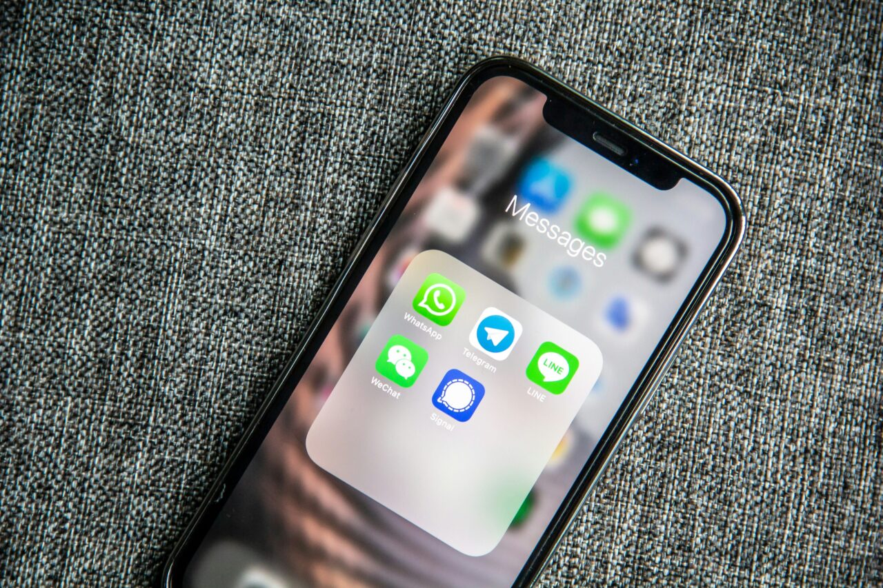 Smartfon z widocznym ekranem zawierającym ikony aplikacji do komunikacji, takich jak WhatsApp, Telegram, WeChat, Signal i LINE, położony na szarej tkaninie.