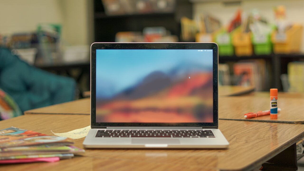 Laptop wyświetlający pulpit. Sprzęt leży na drewnianym stole obok kleju i kredek.