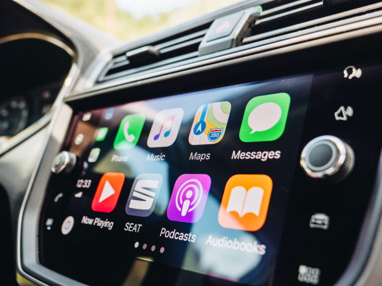 Ekran systemu multimedialnego Apple CarPlay w samochodzie z wyświetlonymi ikonami popularnych aplikacji, takich jak Telefon, Muzyka, Mapy, Wiadomości, Podcasty i Audiobooki.