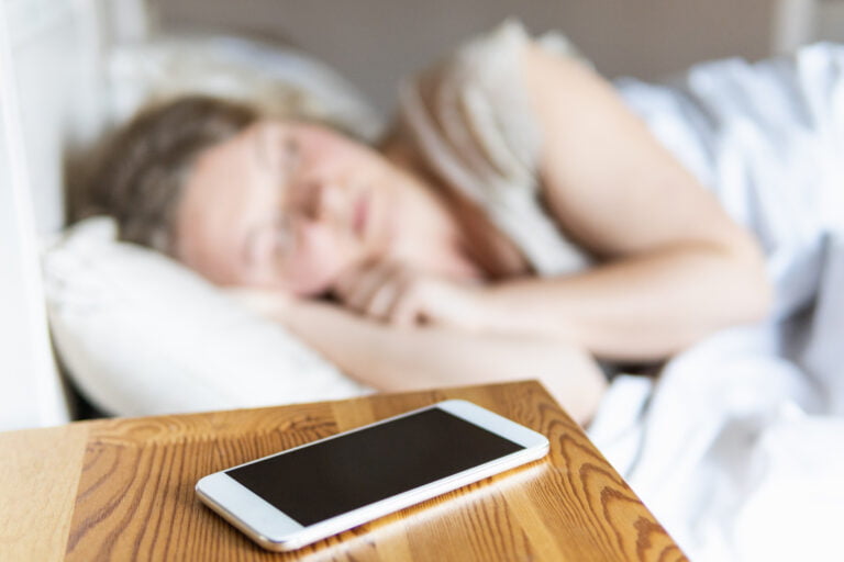 smartfon na półce nocnej w tle jest widoczna śpiąca kobieta
