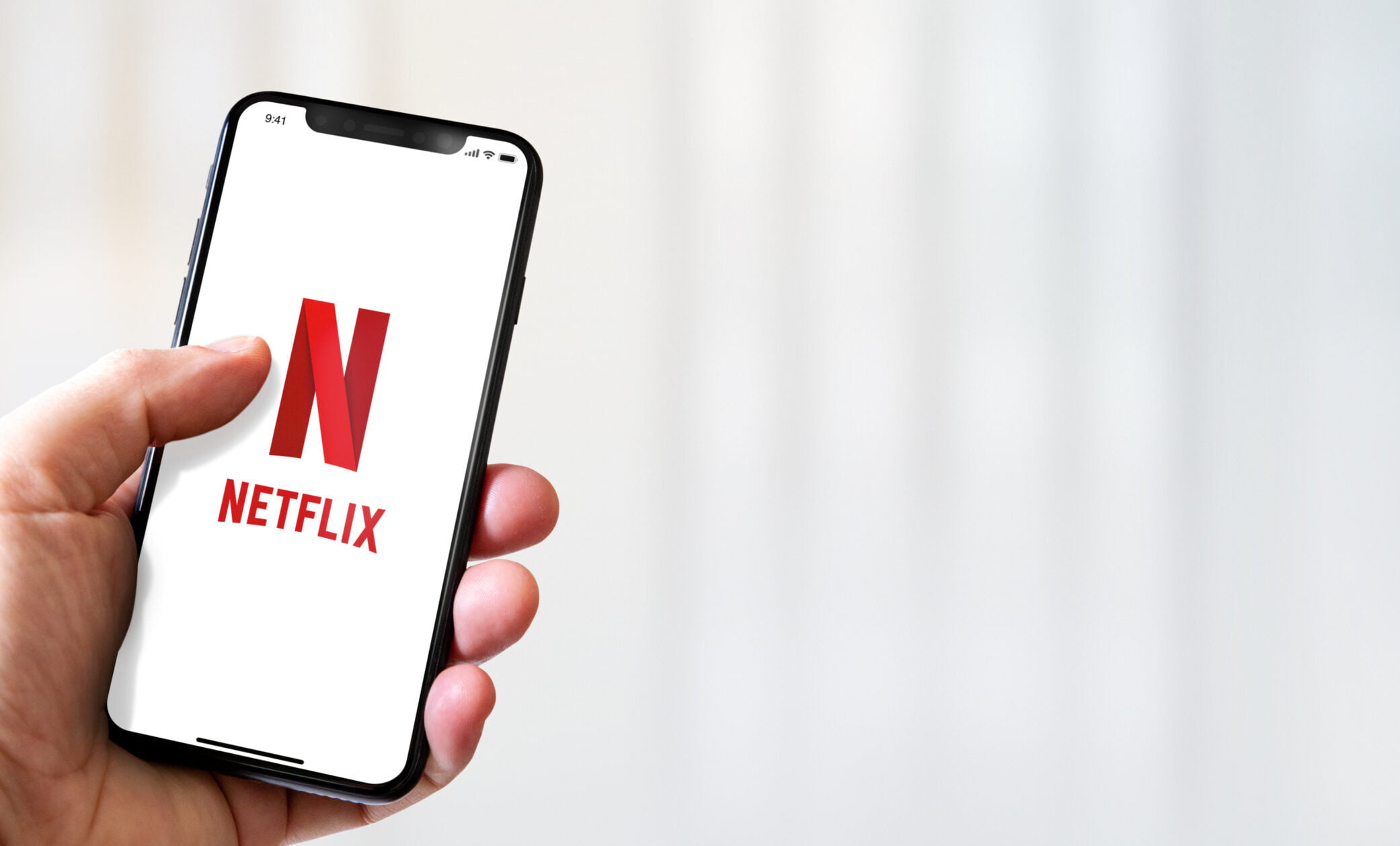 Logo Netflix na smartfonie trzymanym przez mężczyznę, w tle jasna tapeta