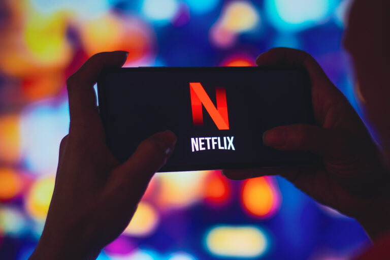 Logo Netflix na smartfonie, w tle migający ekran telewizjny