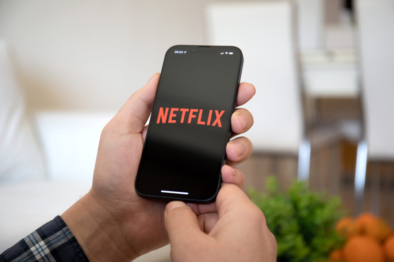 Logo Netflix na smartfonie, telefon trzyma mężczyzna w średnim wieku