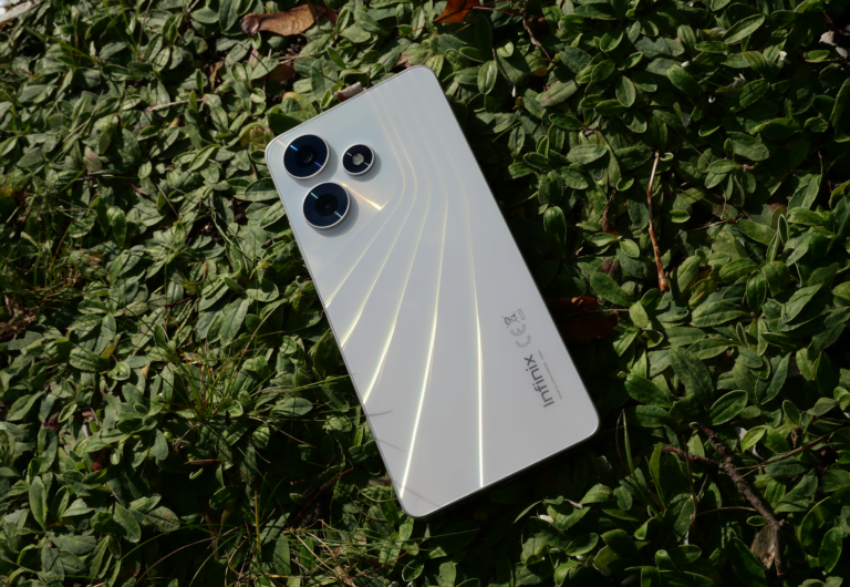 Biały smartfon Infinix HOT 30 leżący na trawie i roślinach