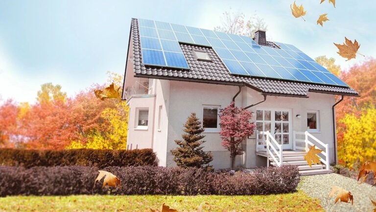 Dom jednorodzinny z panelami słonecznymi na dachu, otoczony kolorowymi drzewami jesienią.