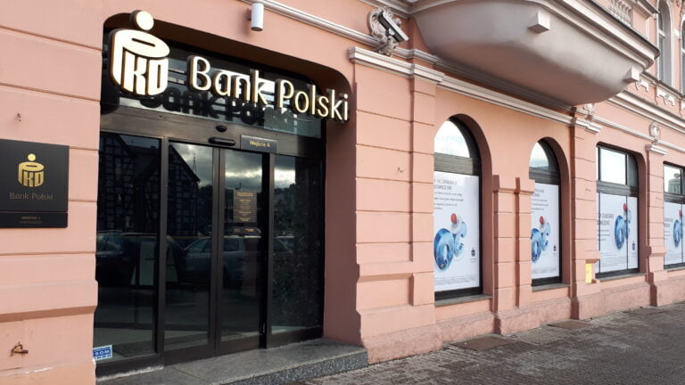 Wejście do oddziału PKO Banku Polskiego z logiem firmy umieszczonym nad drzwiami i plakatami na witrynach.