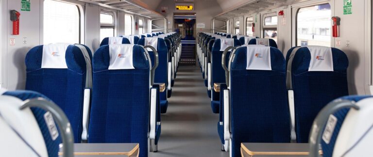 Wnętrze pociągu z rzędami niebieskich siedzeń i przejściem pośrodku.