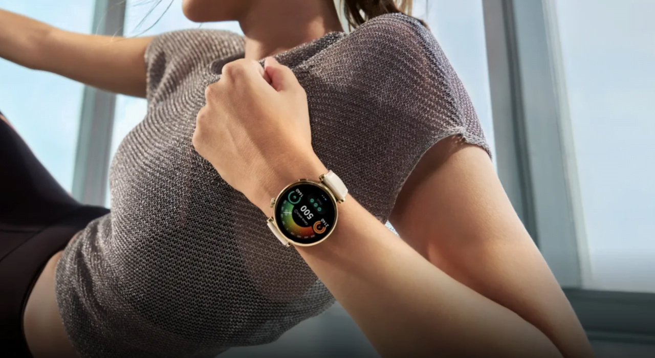 Kobieta zegarek typu smartwatch na nadgarstku, wyświetlający kolorowy interfejs ze wskaźnikami fitness.