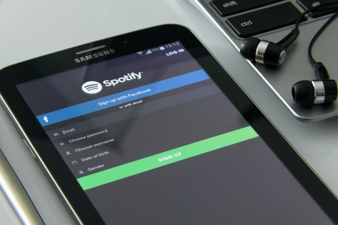 Smartfon Samsung leżący na laptopie, wyświetlający ekran rejestracji w aplikacji Spotify, obok słuchawki douszne.
