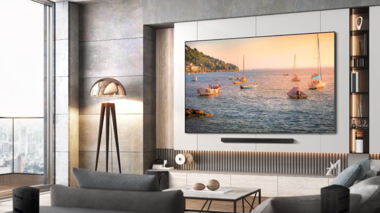 telewizor Samsung 98Q80C z soundbarem w pokoju. telewizor wisi na ścianie a na ekranie widać obraz łódek na jeziorze