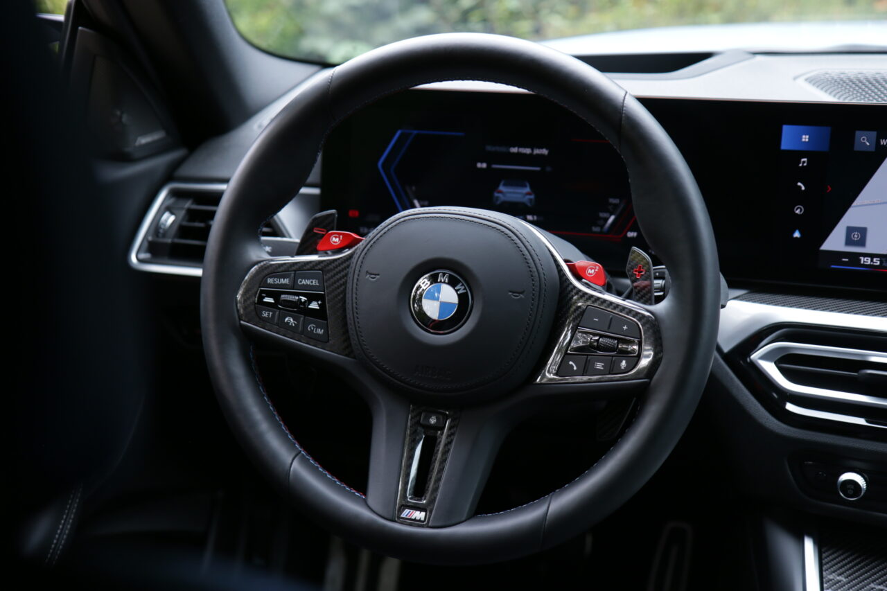 Kierownica testowanego BMW M2 wykończona włóknem węglowym, z czerwonymi przyciskami M1 i M2.
