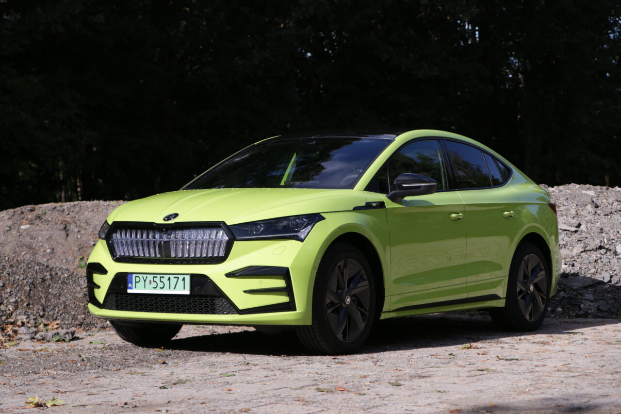 Zielony samochód osobowy marki Škoda zaparkowany na żwirowej drodze z drzewami w tle.