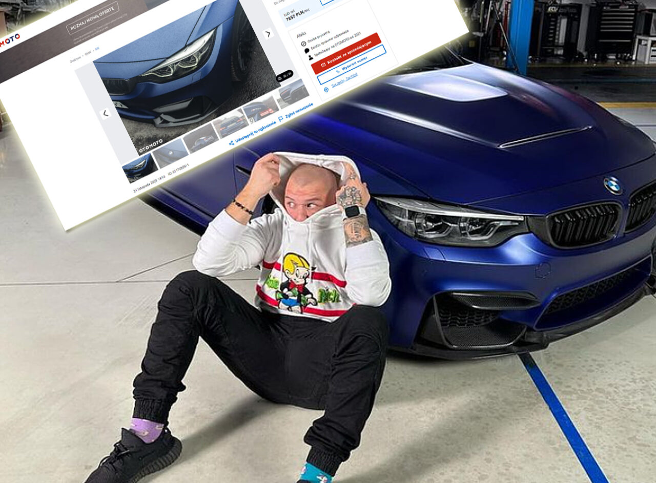 Loteria 7 aut. Budda w bluzie z kapturem i spodniach siedzi na podłodze w warsztacie samochodowym, z jedną ręką ciągnącą kaptur na głowie; w tle widoczny niebieski samochód BMW M3 i zrzutowy ekran komputera z otwartą stroną internetową.