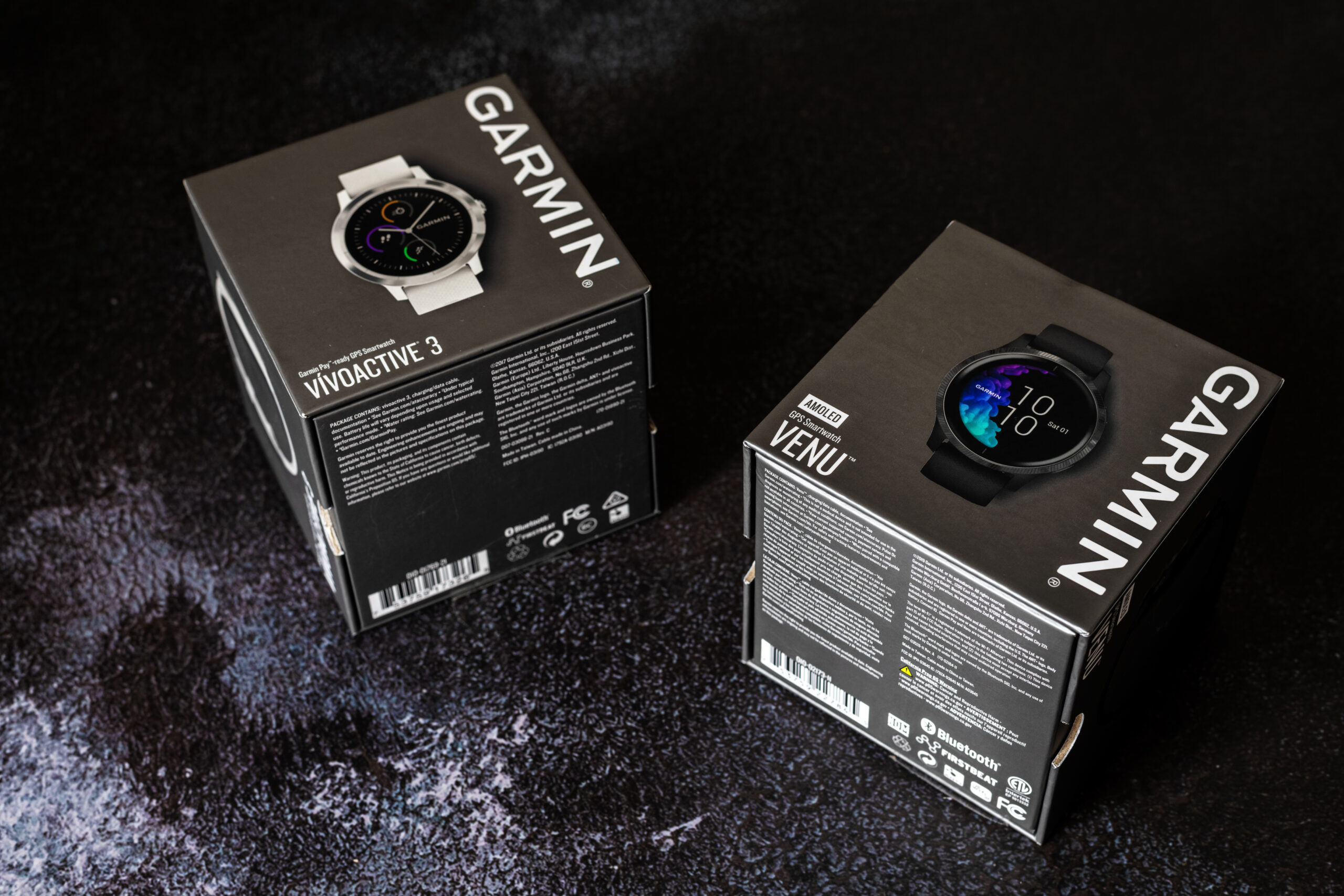 Dwa smartwatche Garmin w pudełku leżące na płótnie - widoczne są modele Garmin Venu i Garmin Vivoactive 3