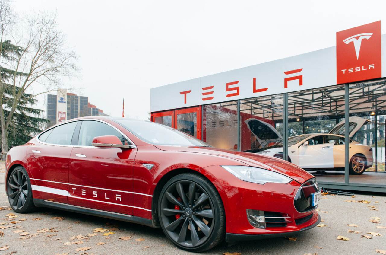 Samochód elektryczny Tesla, elektryk tesla na tle salonu Tesla z wyraźnie widocznym logotypem firmy.