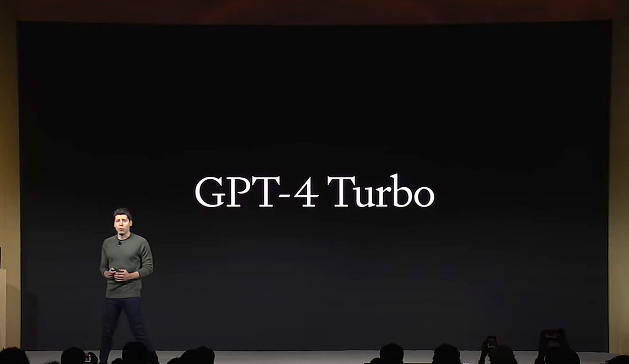 Sam Altman po lewej stronie a za jego plecami czarny ekran, na którym widać napis GPT-4 Turbo