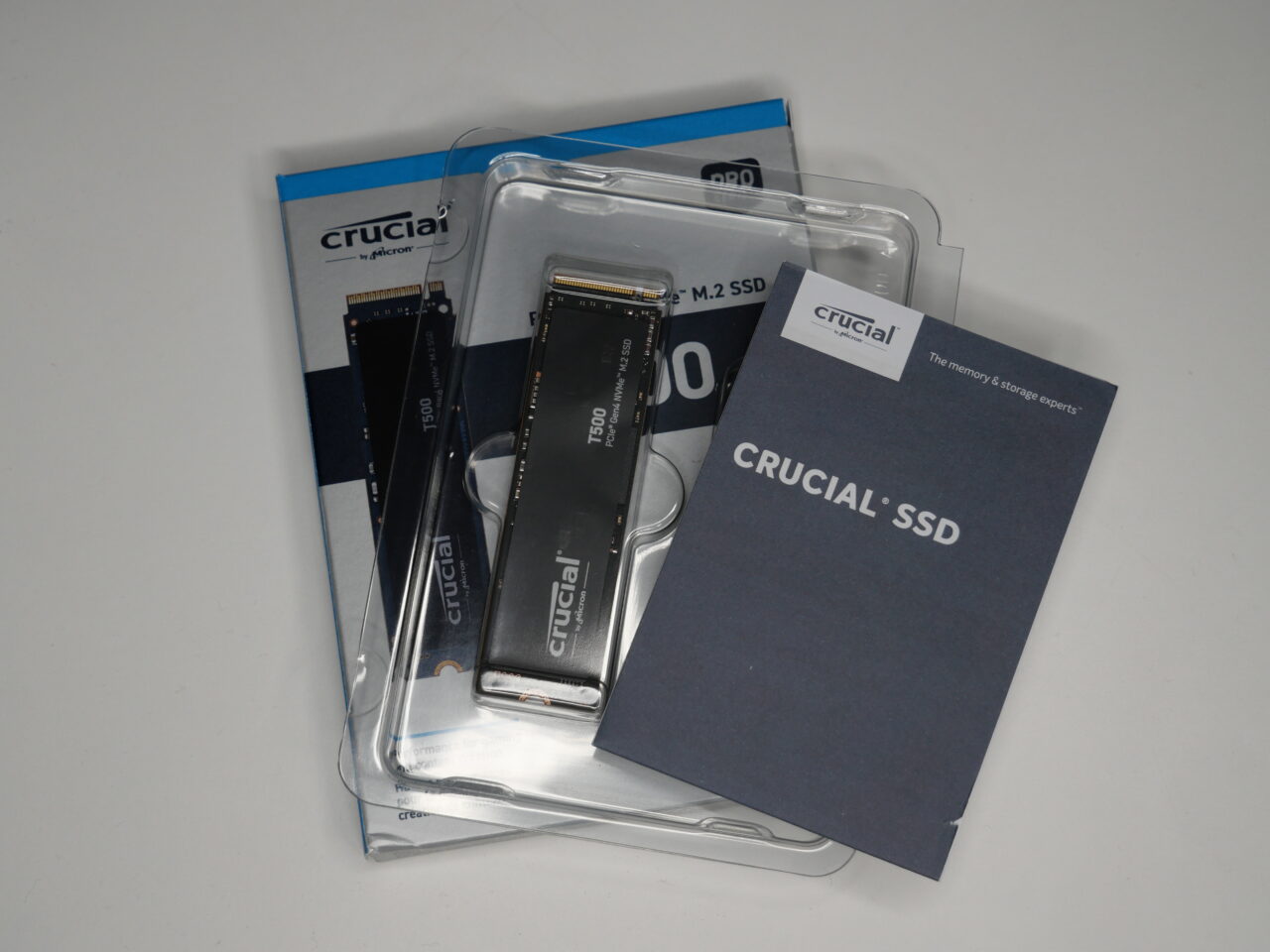 Dysk SSD marki Crucial leżący obok opakowania i instrukcji użytkownika na białym tle.