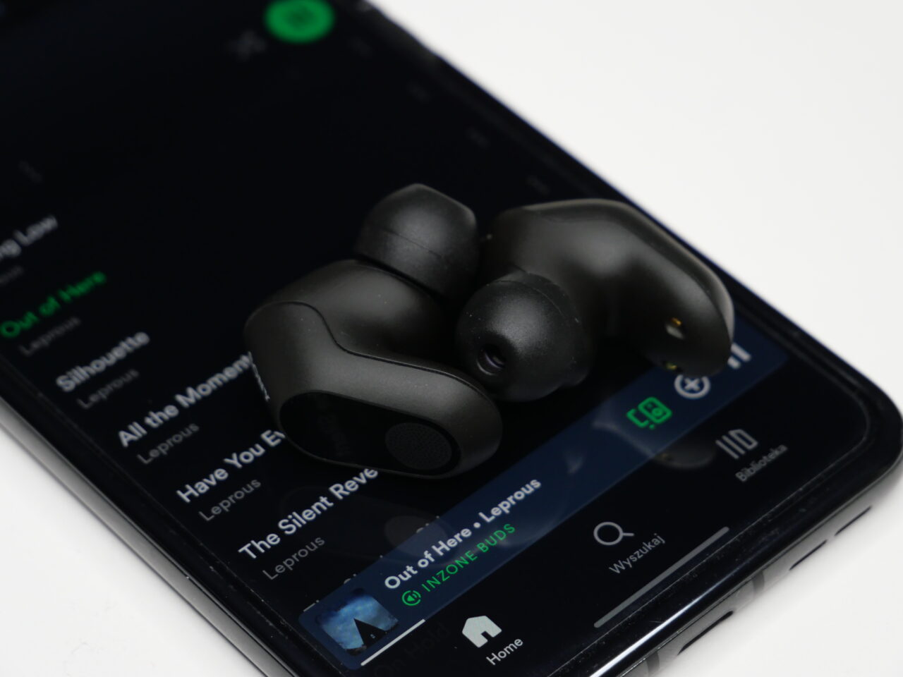 Apple Music vs Spotify. Czarne słuchawki Sony INZONE Buds na smartfonie odtwarzającym muzykę