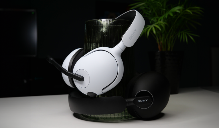 Białe słuchawki nauszne marki Sony INZONE H5 i Sony Inzone H9 z mikrofonem, oparte o ciemne, szklane naczynie, na tle z rośliną w doniczce i ciemnym wnętrzem.