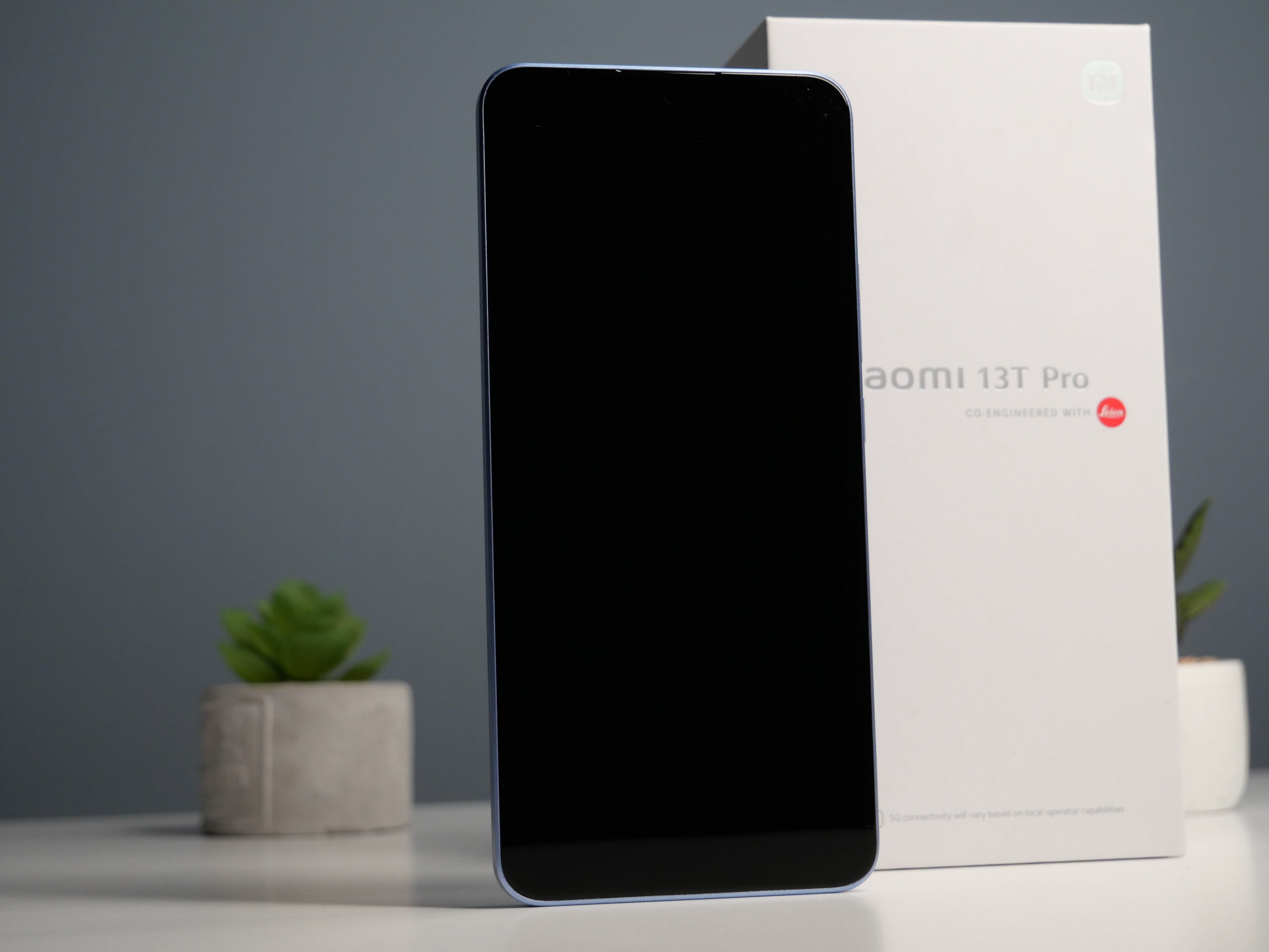 Front smartfona Xiaomi 13T Pro, w tle pudełko i ciemna ściana